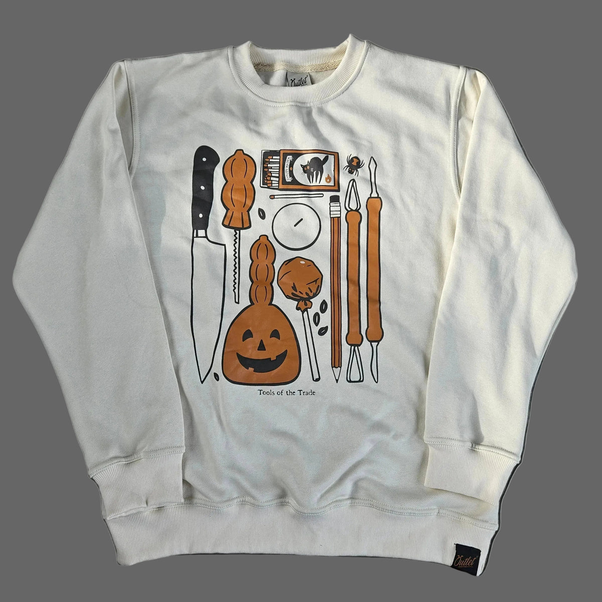 An off-white long-sleeve sweatshirt laid flat on a gray concrete surface, featuring a graphic print of various carving tools.